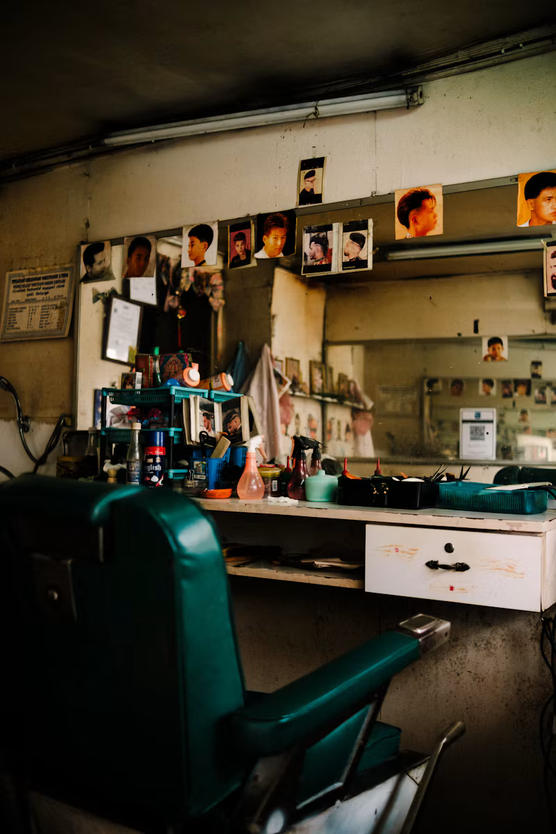 A green barber chair in front of a mirror lined with haircut photos.
